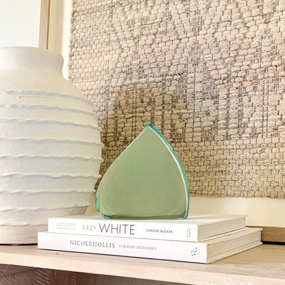 Abstract green glass sculpture with smooth, curved edges displayed on design books