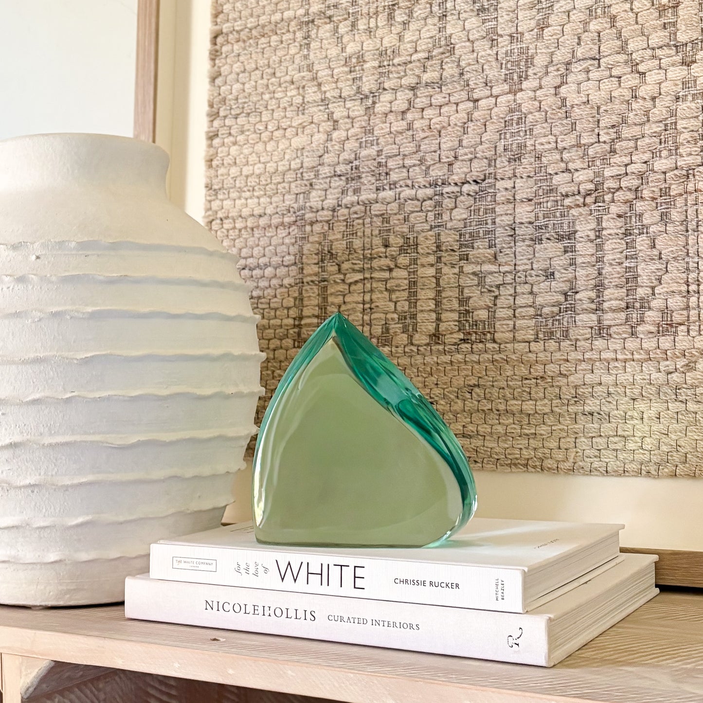 Modern green glass art piece resting on stacked interior design books beside a textured white vase