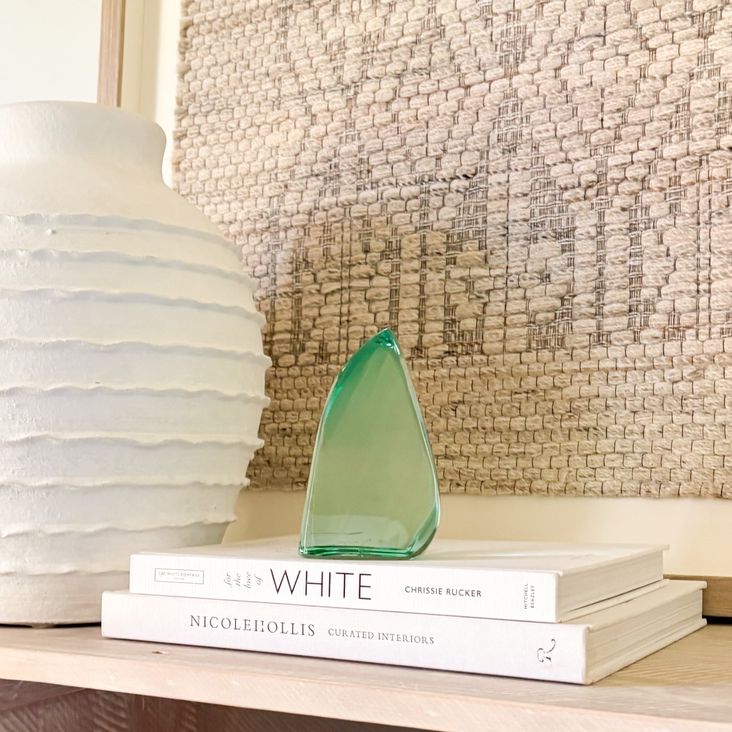 Translucent green glass sculpture styled on a shelf with decor books and a ceramic vase