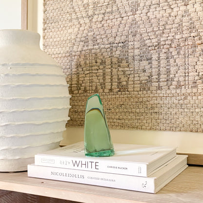 Abstract green glass sculpture with smooth, curved edges displayed on design book