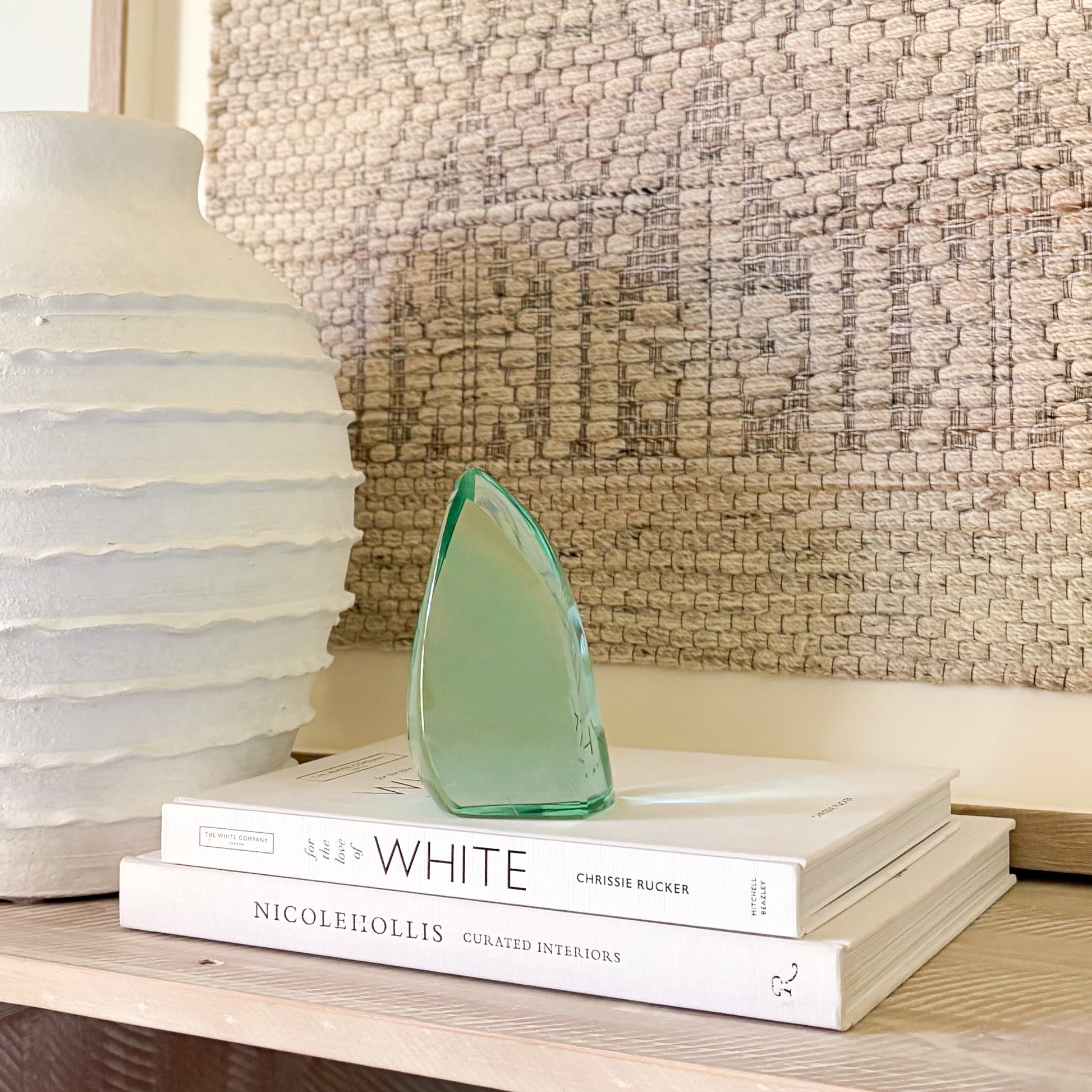 Abstract teal-green glass sculpture with polished surfaces, displayed on books for scale
