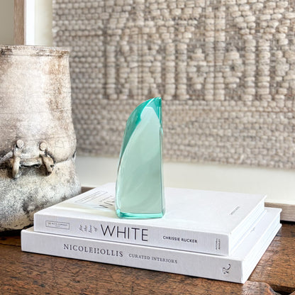 Green glass sculpture displayed on shelf in minimalist modern interior