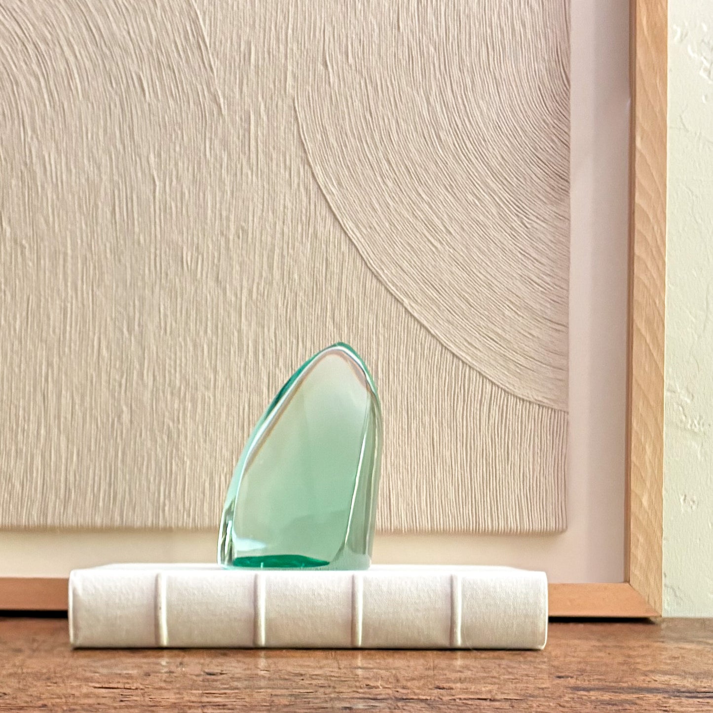 Faceted translucent green glass sculpture with angular design placed on white base against textured wall art