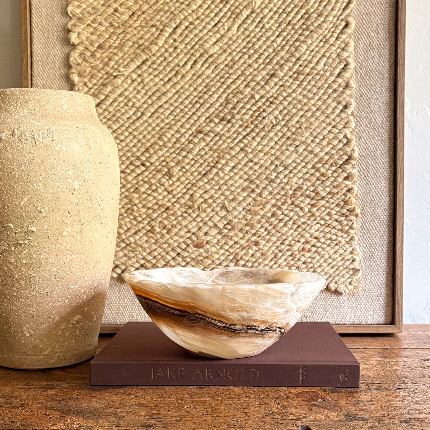 Decorative brown and white onyx bowl on a book with a textured wall and vase in the background