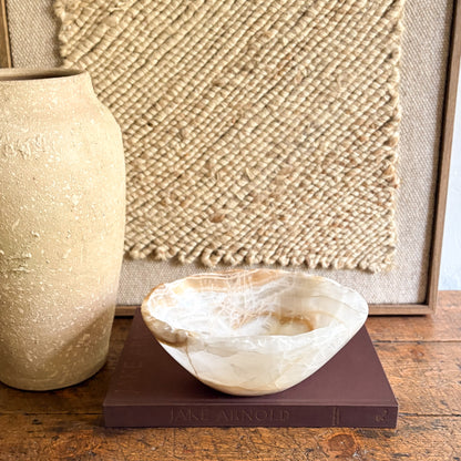 Decorative onyx bowl on a book with a textured wall and vase in the background