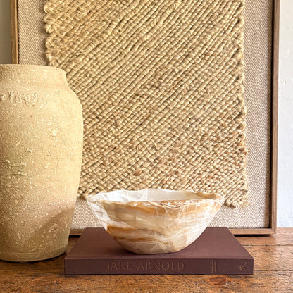 Decorative onyx bowl on a book with a textured wall and vase in the background