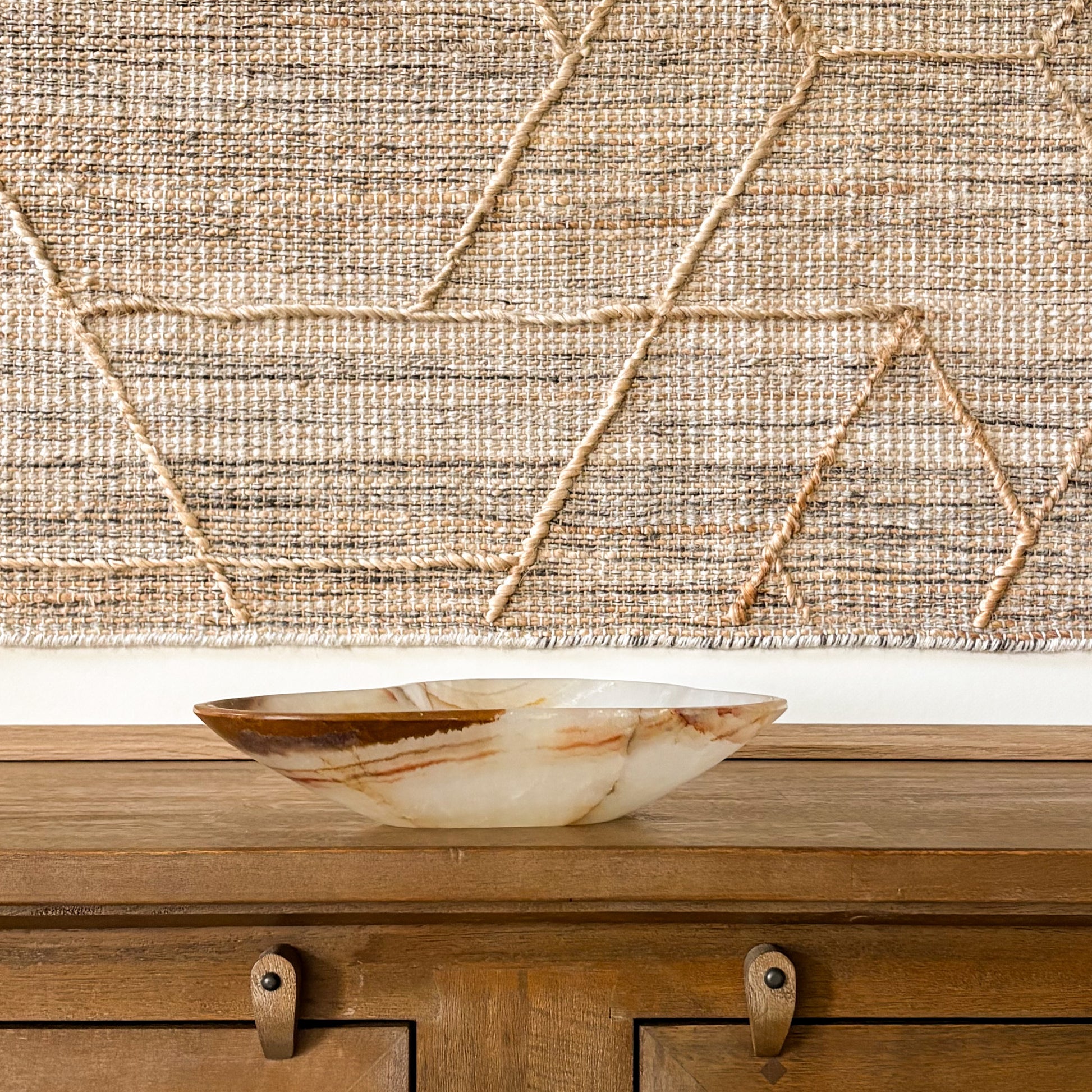 Hand-carved brown onyx bowl on wooden console table with textured wall hanging background