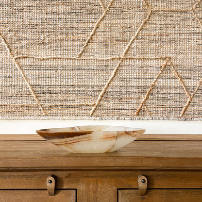 Hand-carved brown onyx bowl on wooden console table with textured wall hanging background