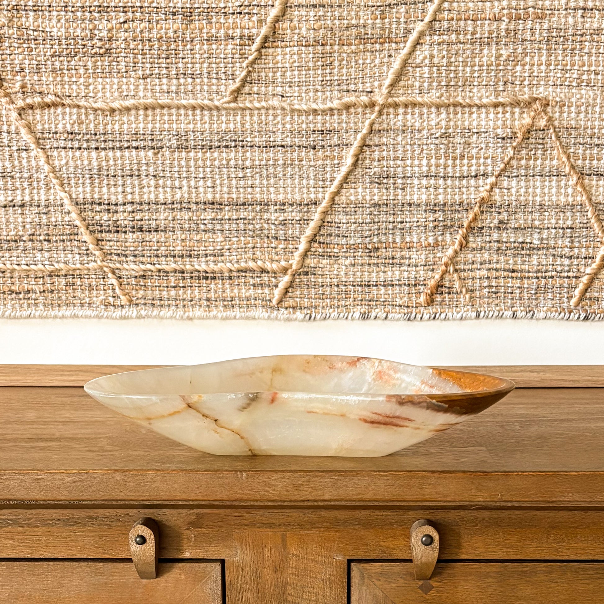 Decorative brown onyx bowl styled on wooden furniture with textured fabric backdrop