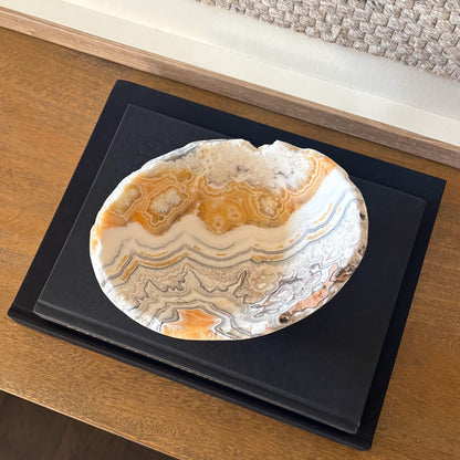 Natural zebra calcite gemstone bowl with gray and amber veining on wooden console