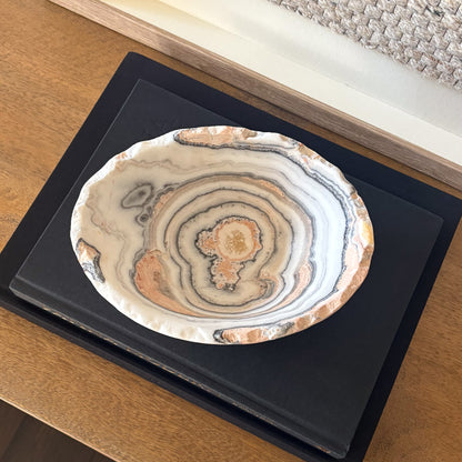 Natural zebra calcite gemstone bowl with gray and amber veining on wooden console