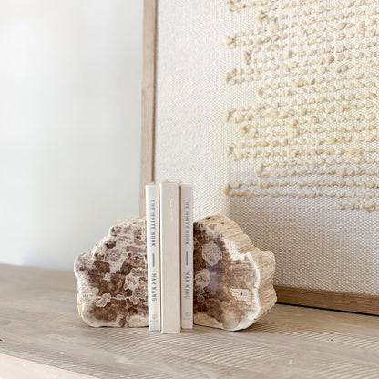 Two books between natural stone bookends on a surface with a textured wall in the background