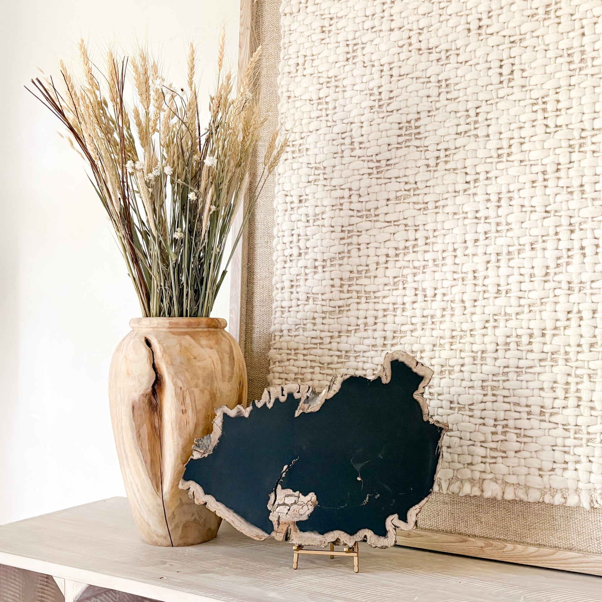 Decorative black petrified wood piece with a wooden vase with dried plants on a light surface.