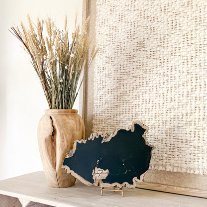 Decorative black petrified wood piece with a wooden vase with dried plants on a light surface.
