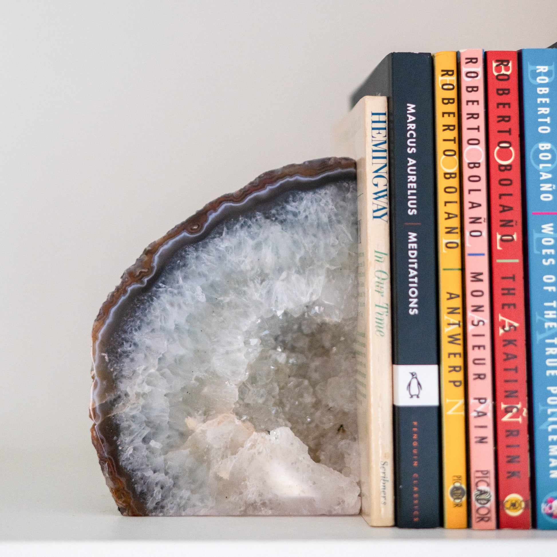 Natural blue Brazilian agate druzy bookends supporting books on a white arched bookshelf in a contemporary home.