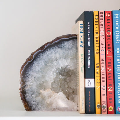 Natural blue Brazilian agate druzy bookends supporting books on a white arched bookshelf in a contemporary home.