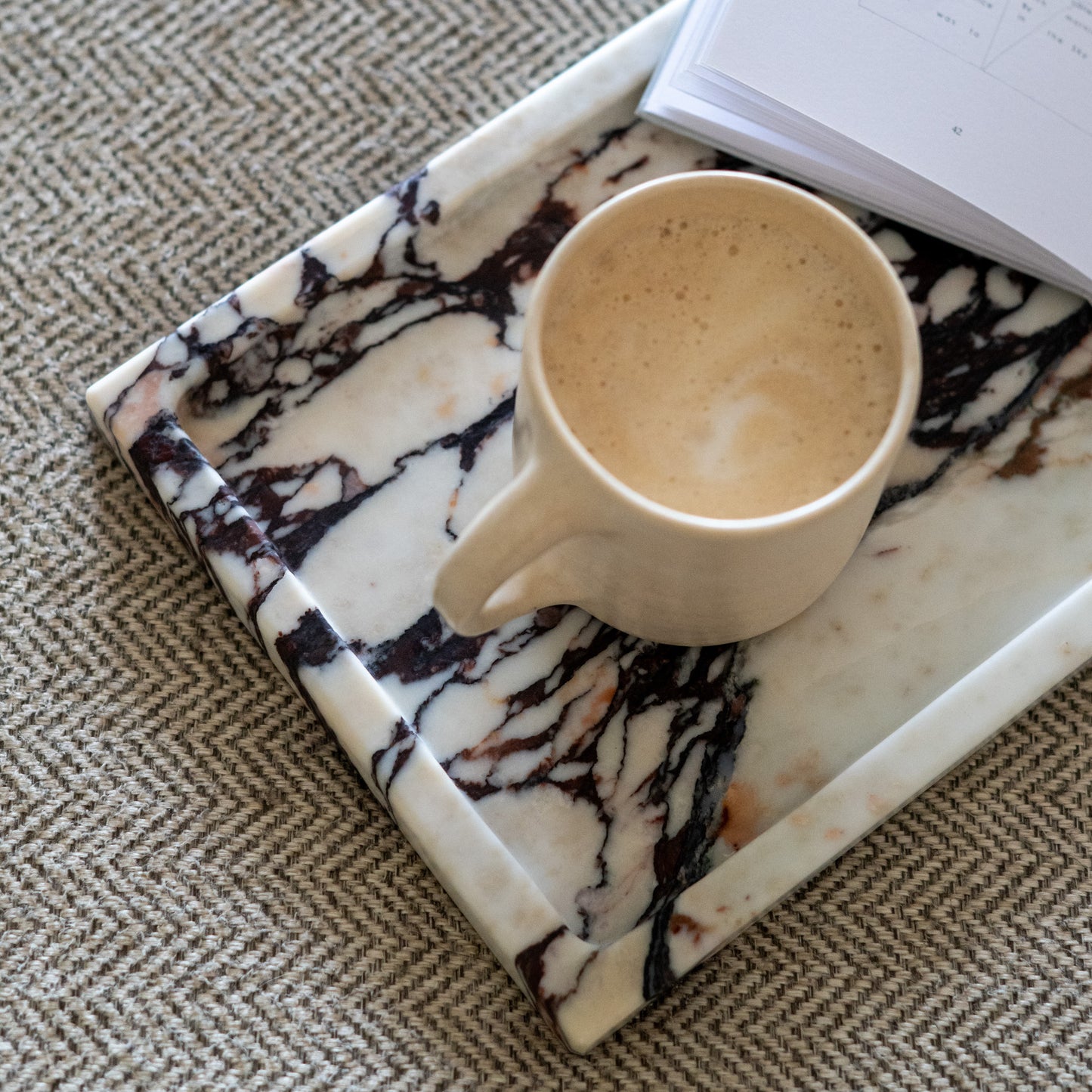 Polished Calacatta Viola marble tray on a couch table with  a coffee cup and a book