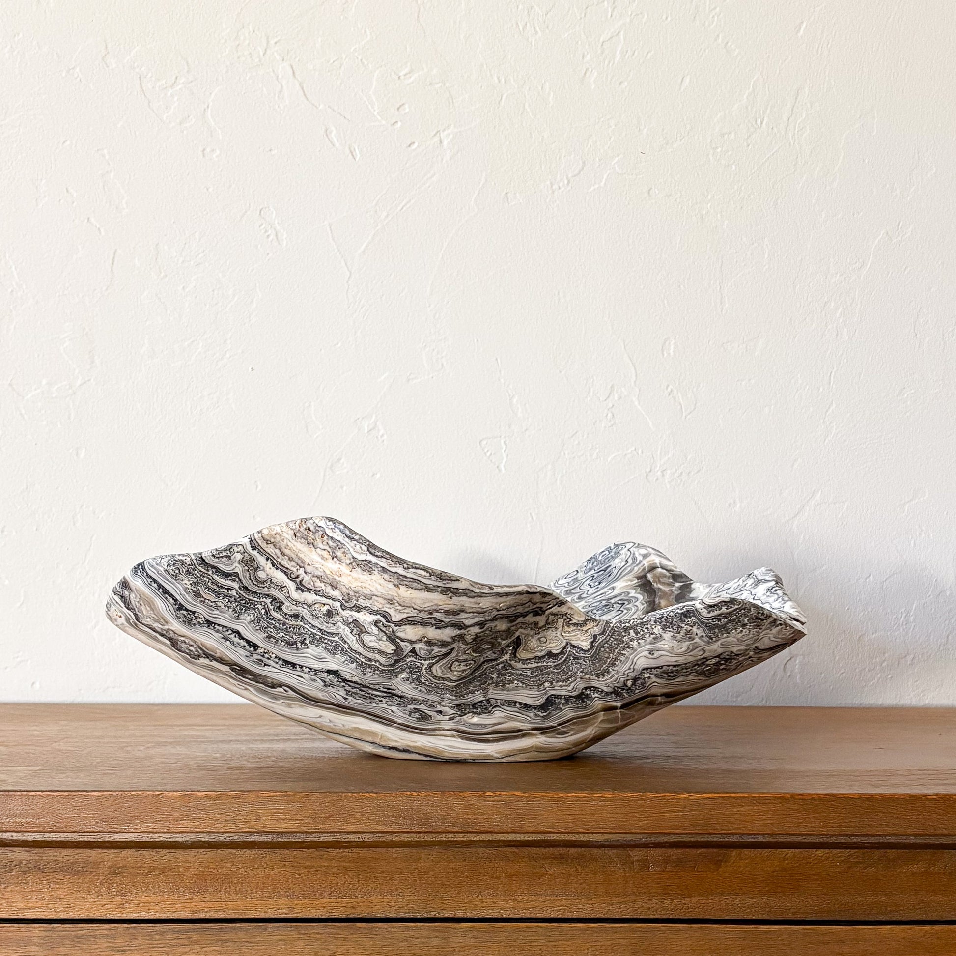 Large hand-carved zebra onyx bowl with dramatic natural banding in cream, gray, and black displayed on a wooden table.