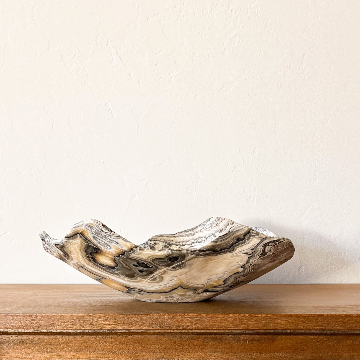 Side view of a sculptural zebra onyx stone bowl with flowing organic edges and natural striped banding.