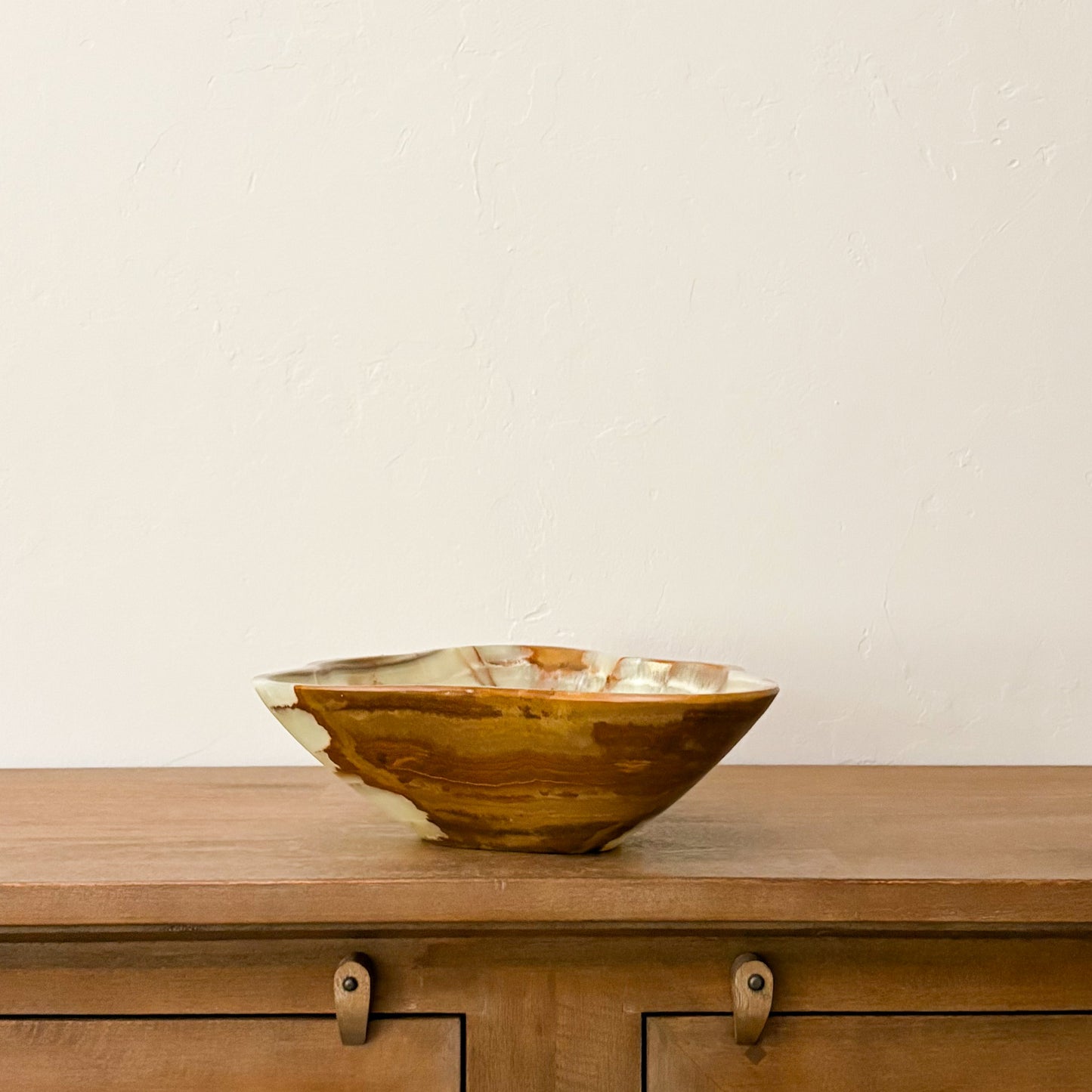 Large hand-carved green onyx bowl with natural cream and brown veining displayed on a wooden cabinet.