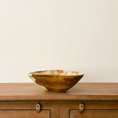 Large hand-carved green onyx bowl with natural cream and brown veining displayed on a wooden cabinet.