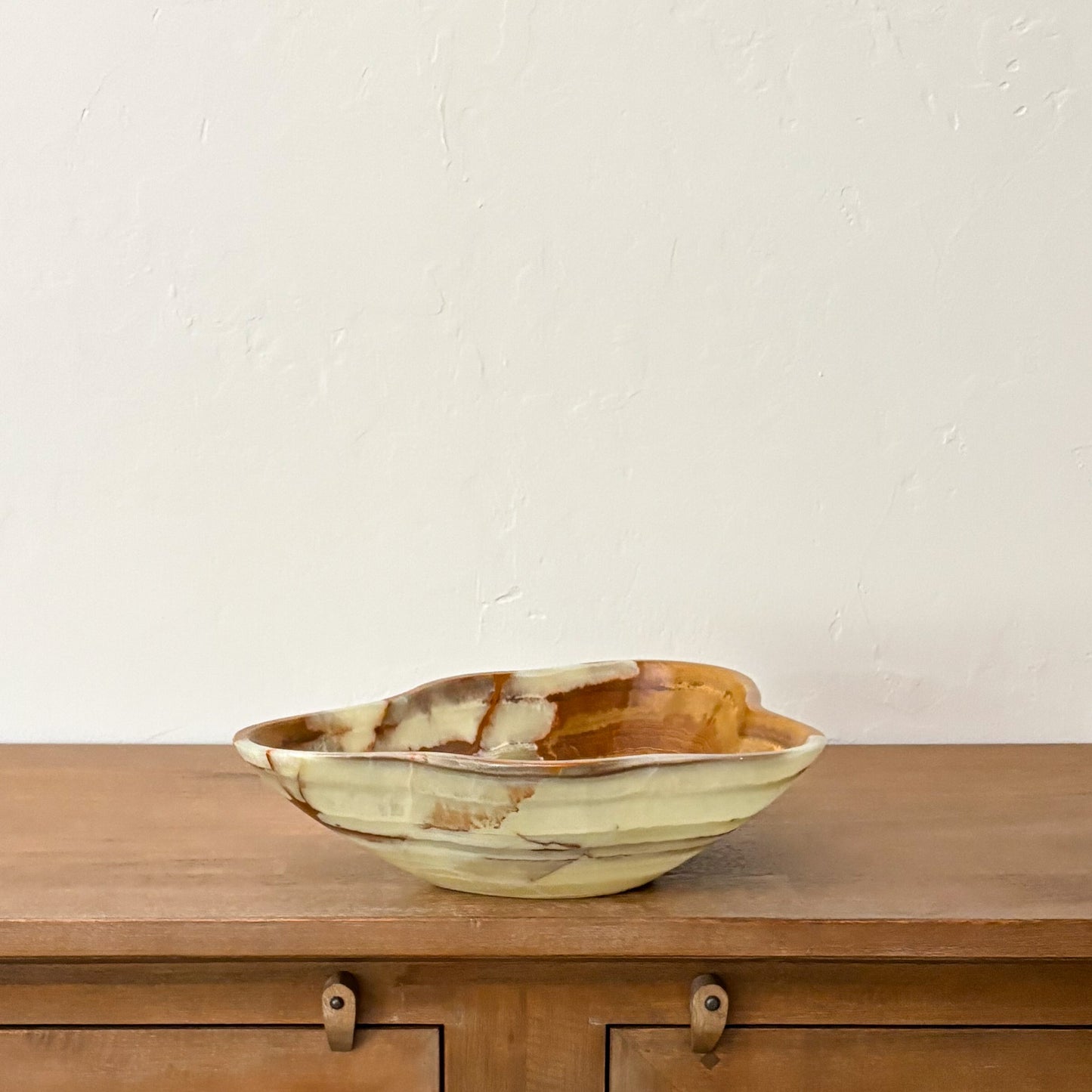 Organic modern green onyx centerpiece bowl styled on a mid-century wooden sideboard against a neutral wall.