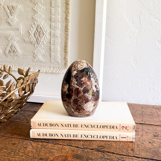 Decorative stone on top of Audubon Nature Encyclopedia books with a textured wall and gold leaf decor in the background.