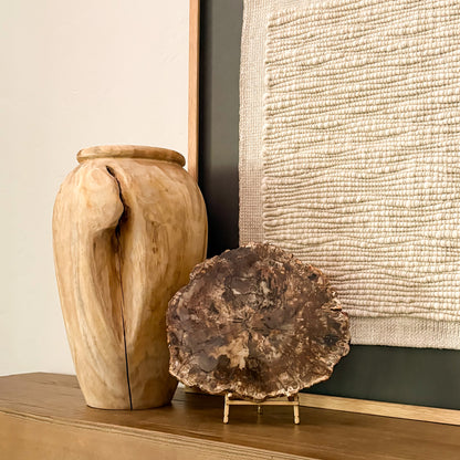 Polished Madagascar petrified wood slab on stand beside handcrafted wooden vase in neutral modern interior