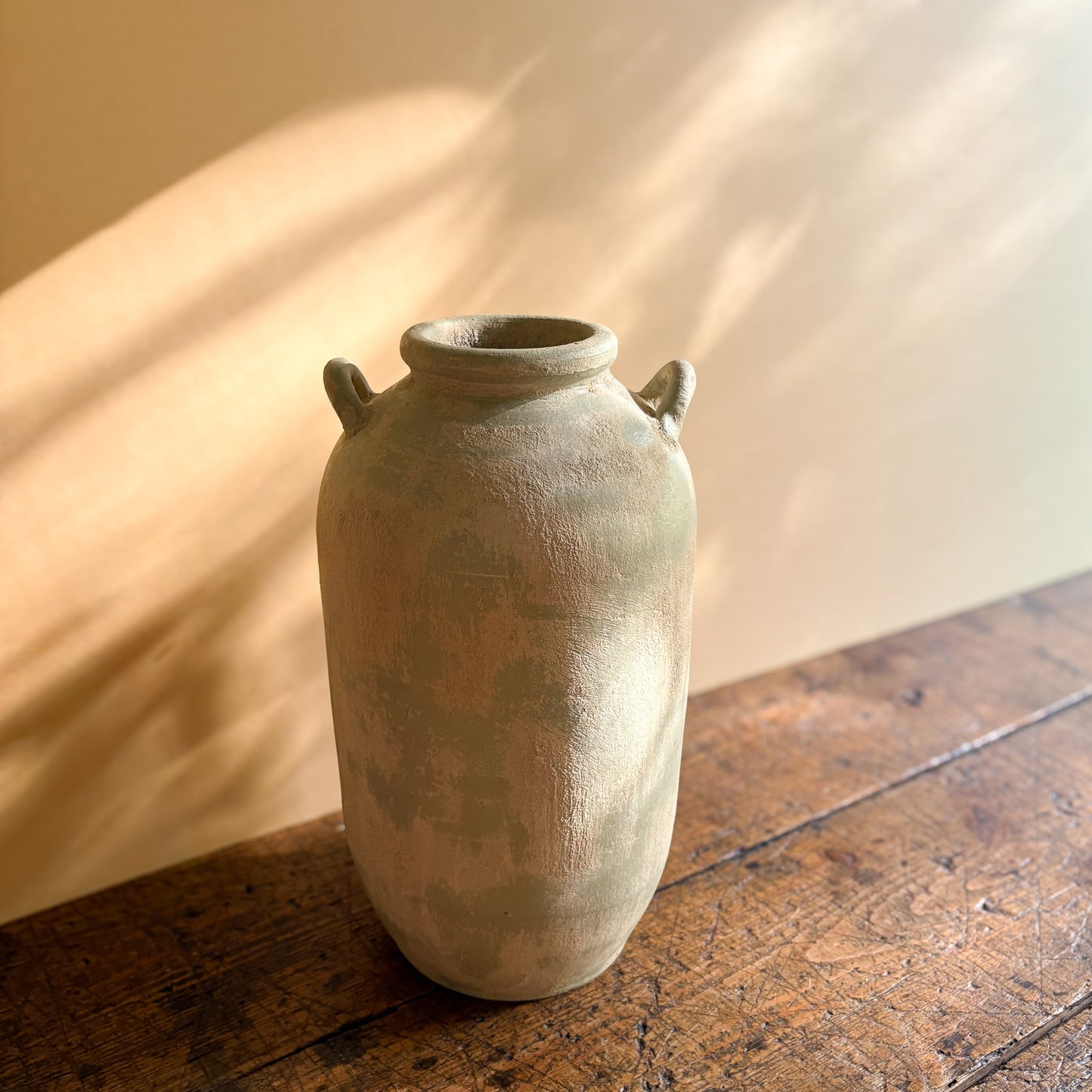 Vintage ceramic vase with two handles on a wooden surface with soft lighting