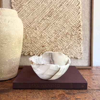 Decorative onyx bowl on a book with a textured wall and vase in the background