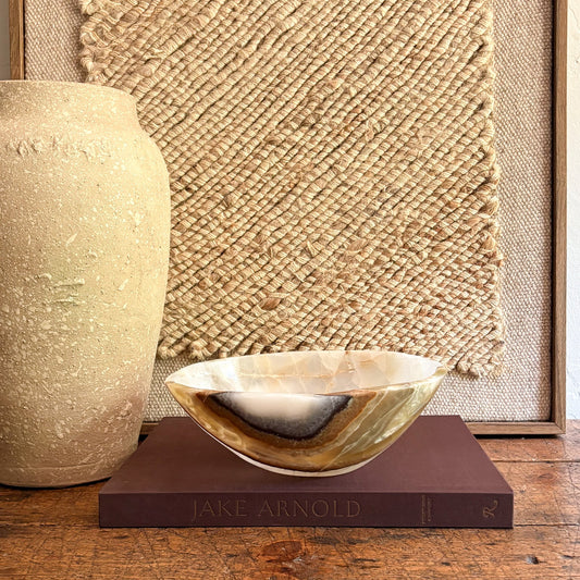 Decorative earth tone onyx bowl on a book with a textured wall and vase in the background