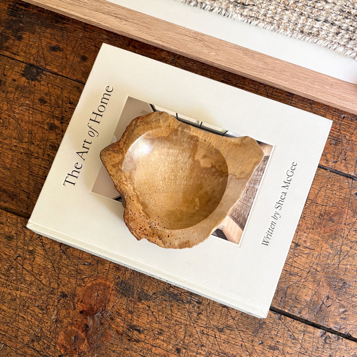 Decorative wooden bowl on a book titled 'The Art of Home' on a wooden surface