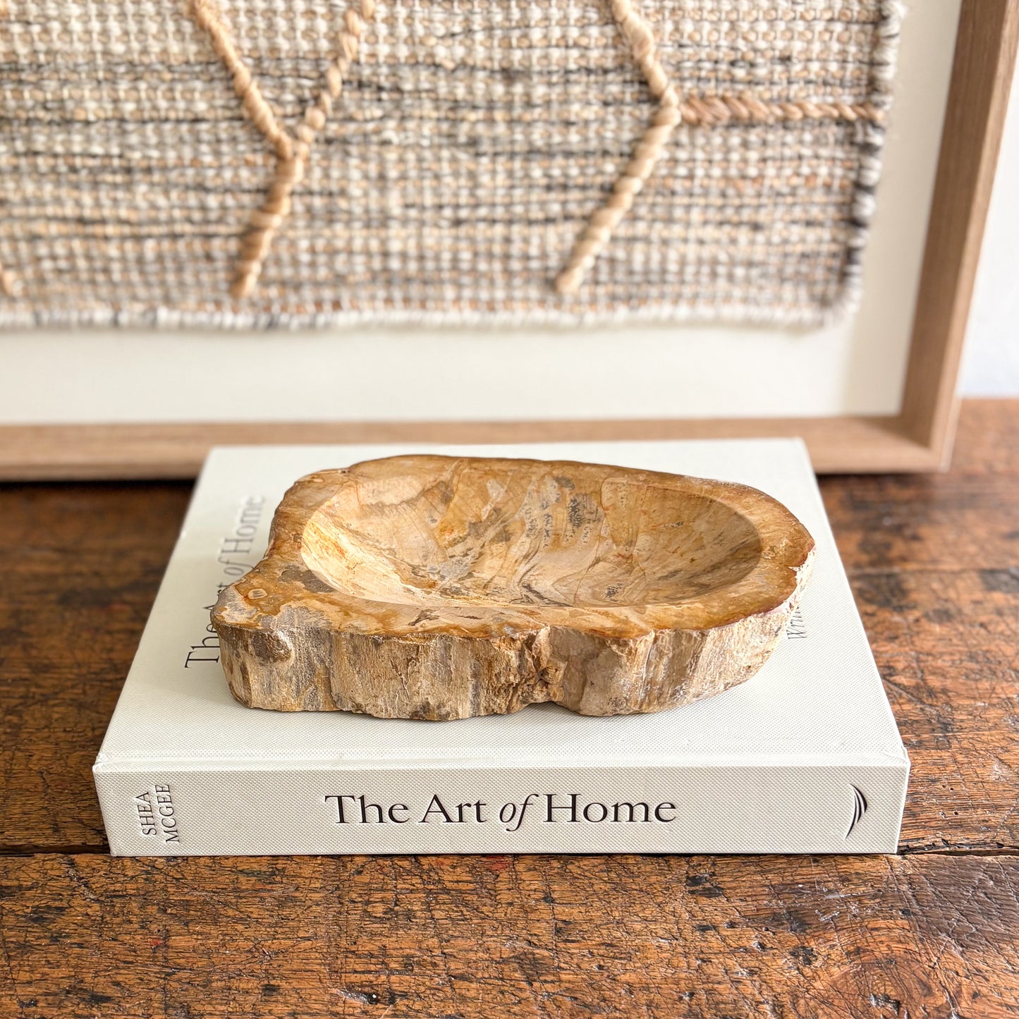 Indonesian petrified wood bowl on a book titled 'The Art of Home' with a textured wall in the background