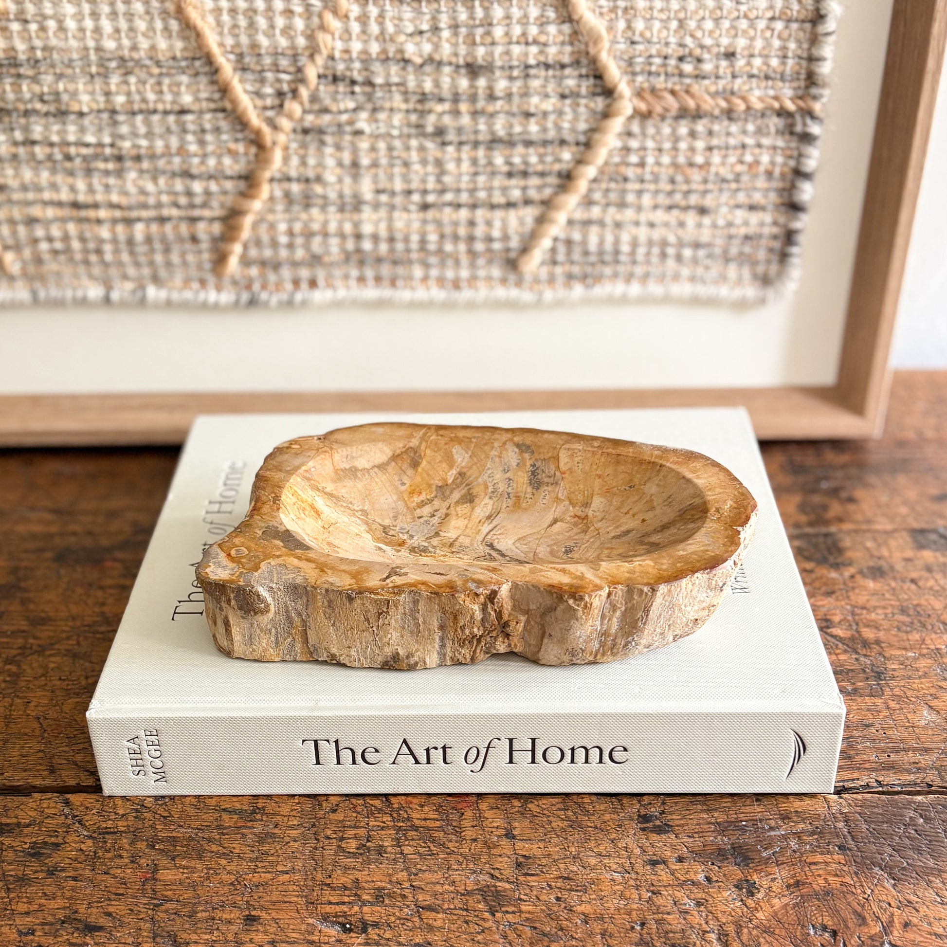 Indonesian petrified wood bowl on a book titled 'The Art of Home' with a textured wall in the background