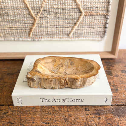 Indonesian petrified wood bowl on a book titled 'The Art of Home' with a textured wall in the background