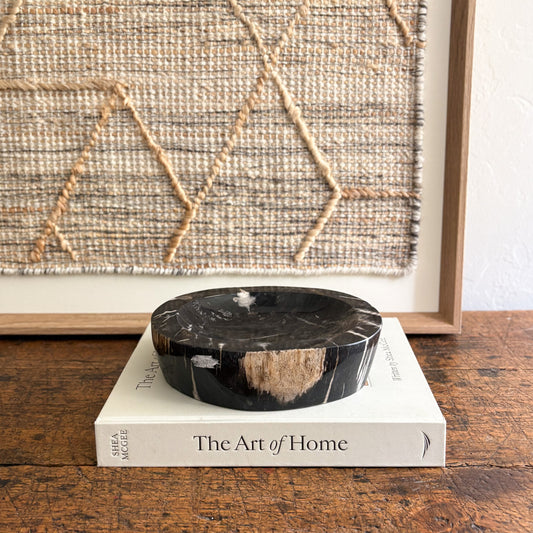 Black indonesian petrified wood bowl on a book titled 'The Art of Home' with a woven wall art in the background.