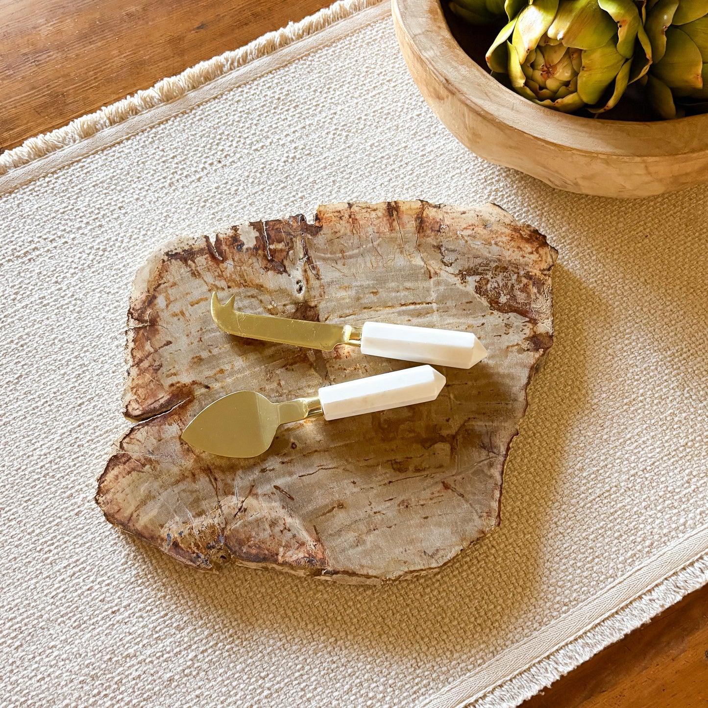 Decorative petrified wood stone platter with gold and white cheese knives on a textured surface.