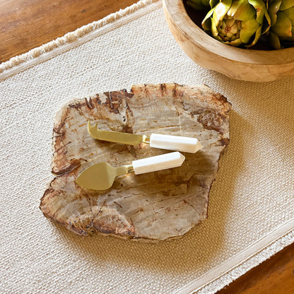 Decorative petrified wood stone platter with gold and white cheese knives on a textured surface.