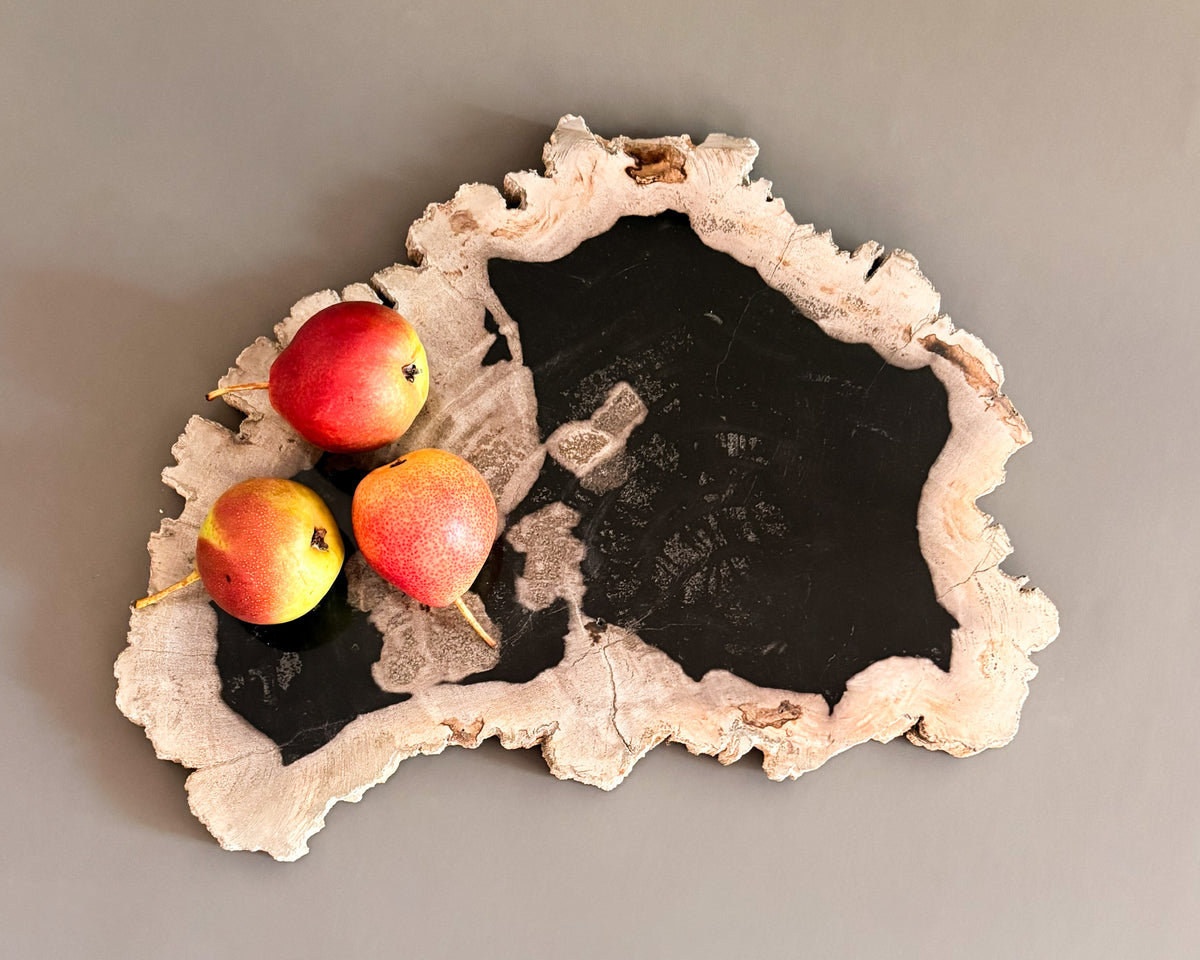 Natural petrified wood serving board with contrasting black center and textured cream edges, styled with three fresh pears.