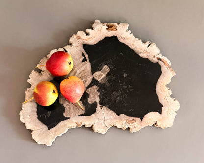 Natural petrified wood serving board with contrasting black center and textured cream edges, styled with three fresh pears.