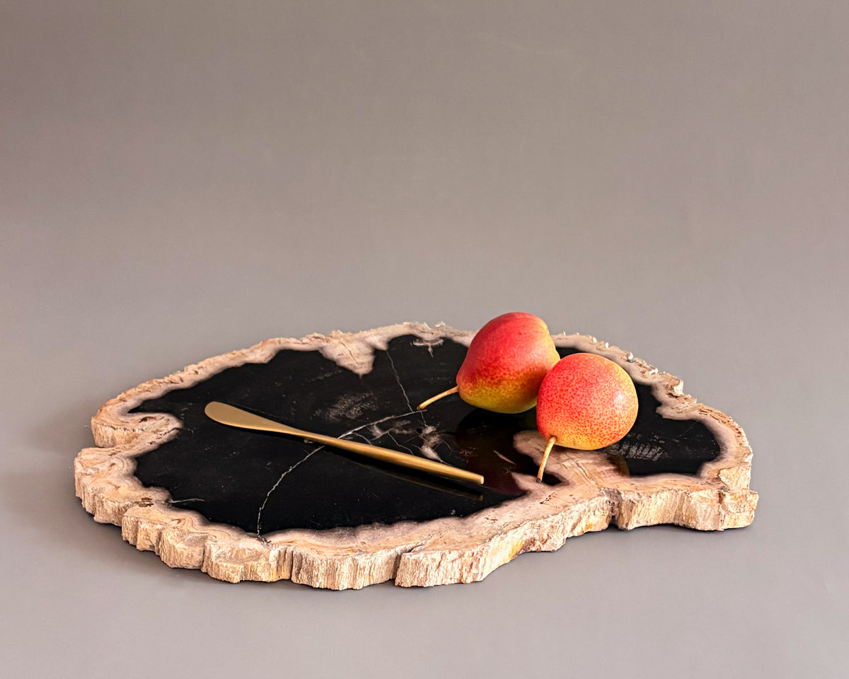 Natural petrified wood serving board with contrasting black center and textured cream edges, styled with fresh pears.