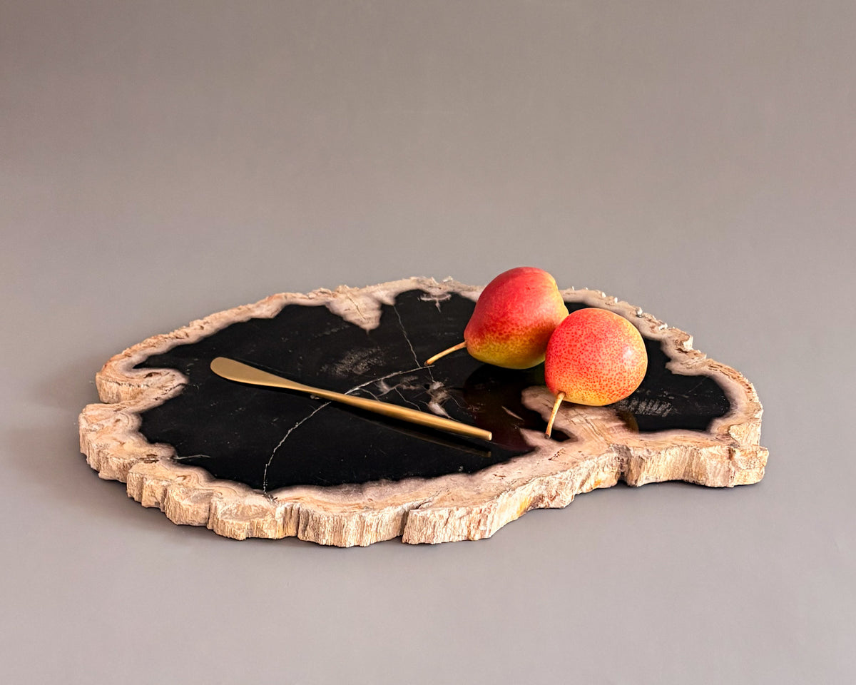Natural petrified wood serving board with contrasting black center and textured cream edges, styled with fresh pears.