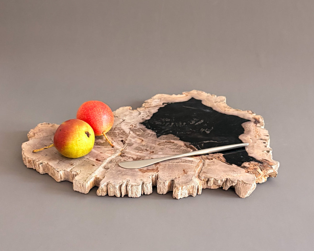 Natural petrified wood serving board with contrasting black center and textured cream edges, styled with fresh pears.