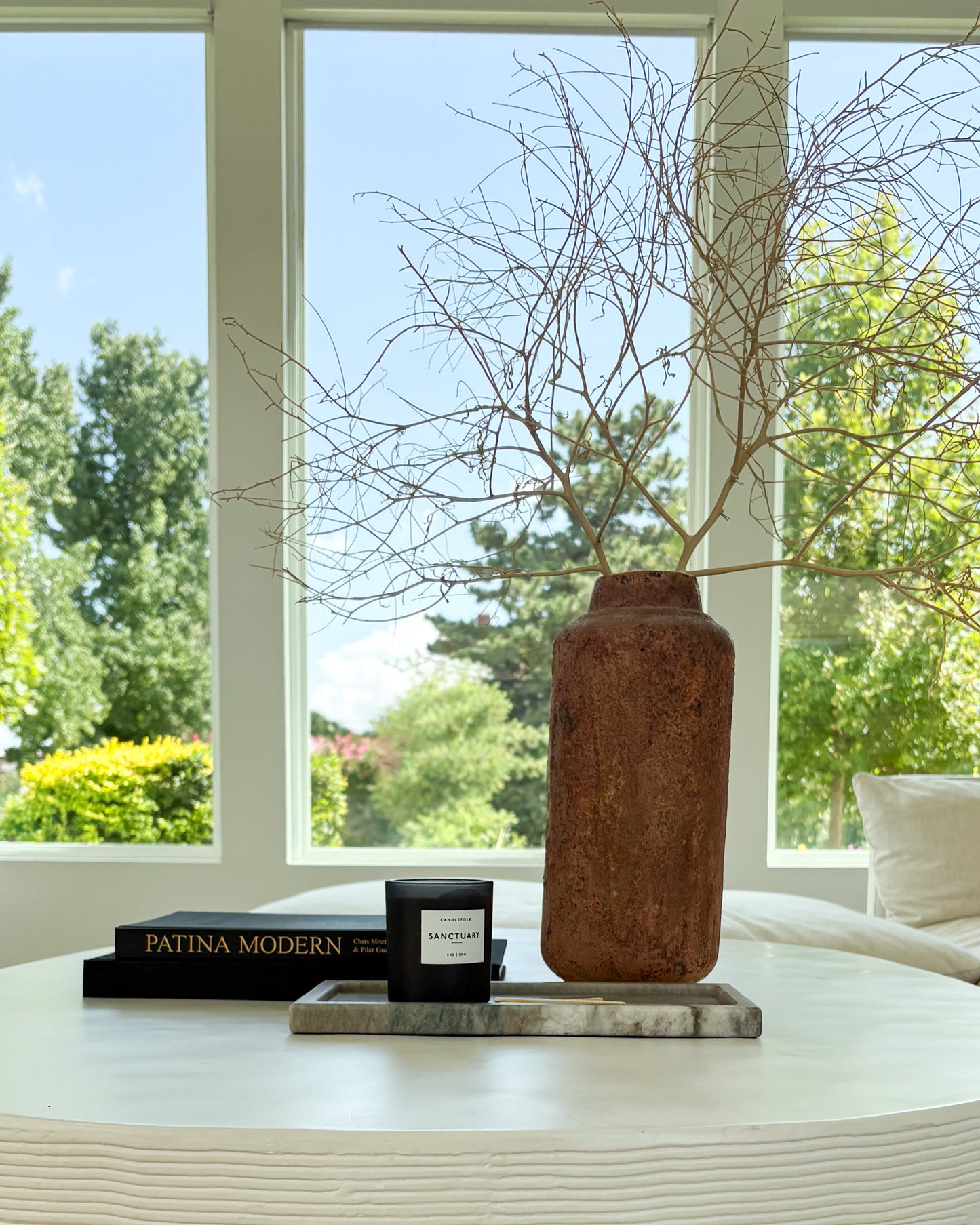 Gray Pocahontas marble tray styled with a black candle on a modern white coffee table with decorative vase and design books