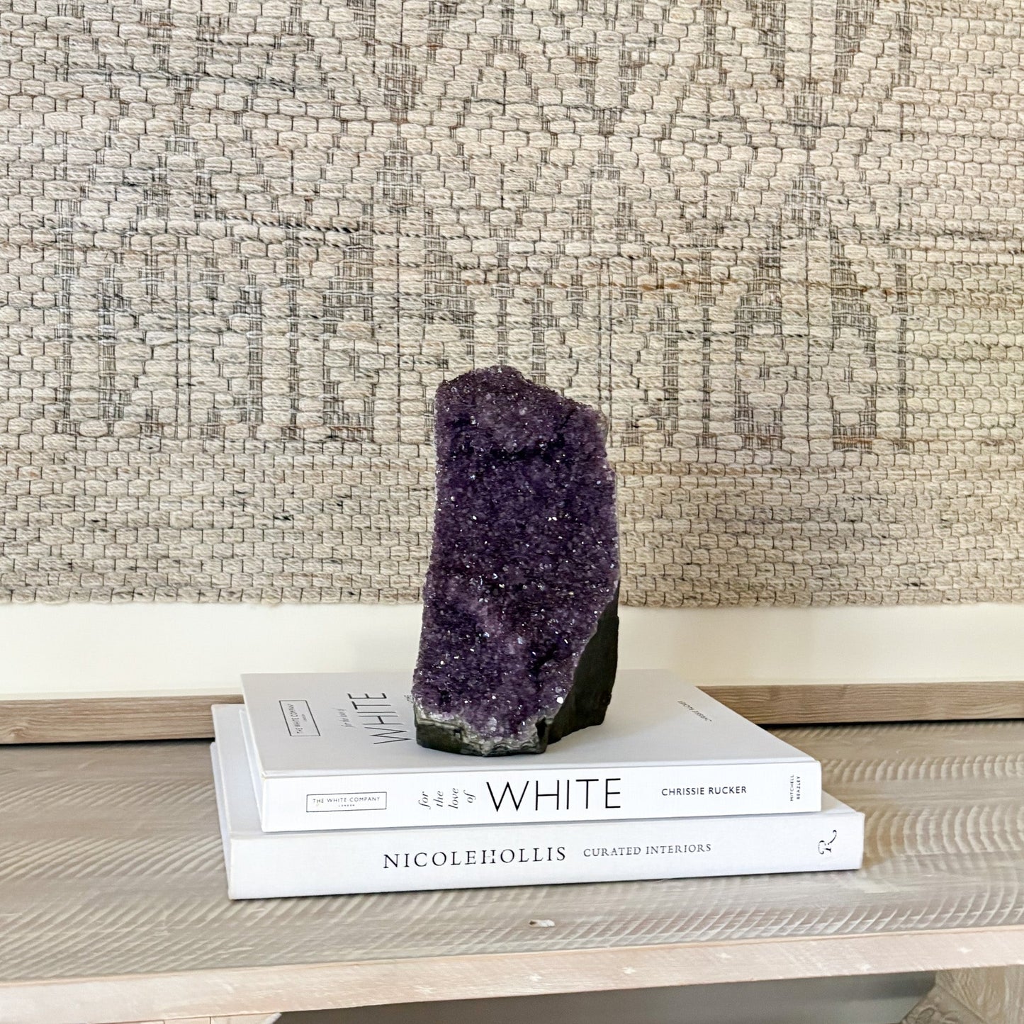 Amethyst crystal on top of two books with a textured wall background
