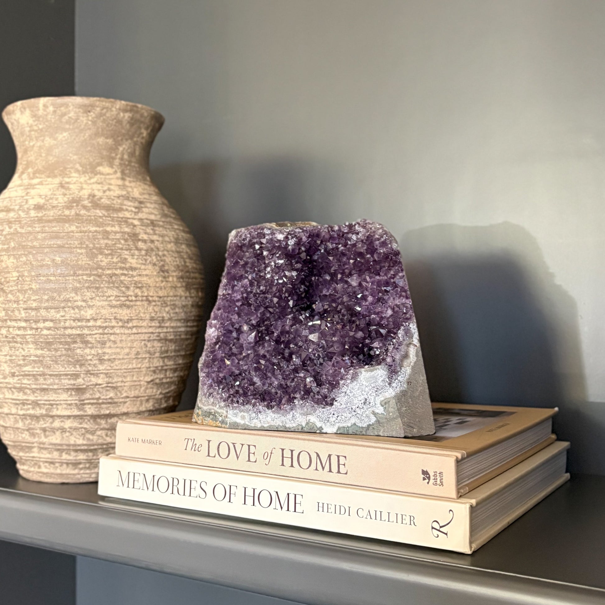 Amethyst crystal on books with a vase next to it against a gray wall