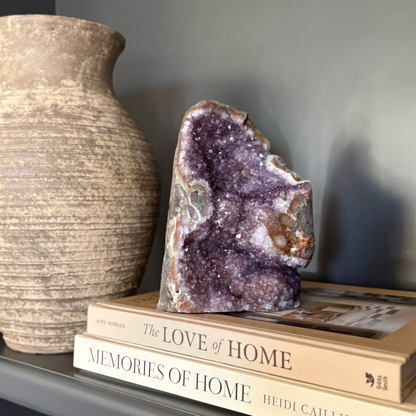 Purple amethyst geode on top of books with a textured vase beside them against a gray background