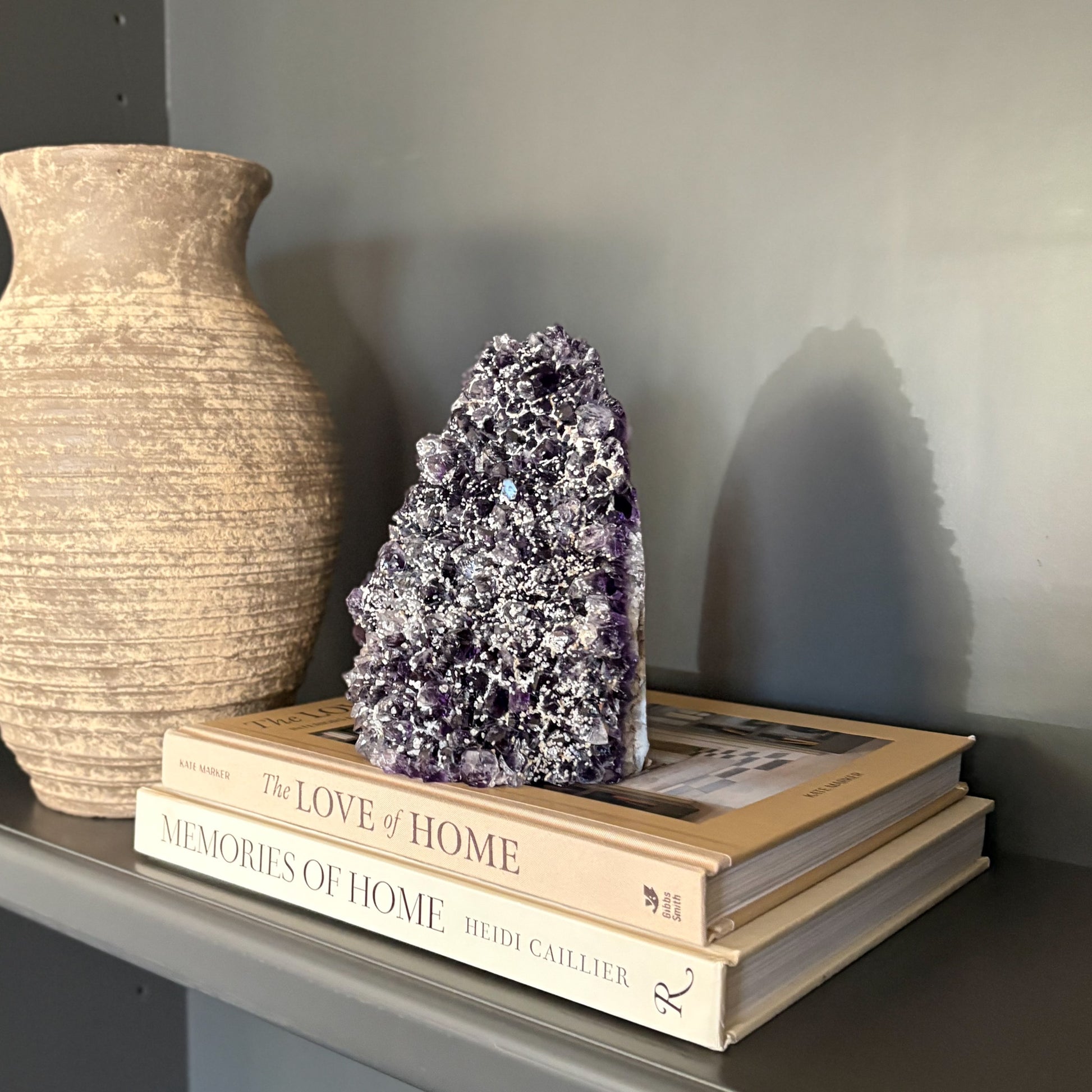 Decorative stack of books with an amethyst crystal sculpture on a shelf next to a vase.