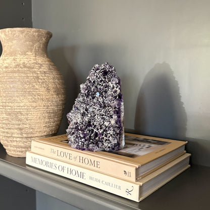 Decorative stack of books with an amethyst crystal sculpture on a shelf next to a vase.