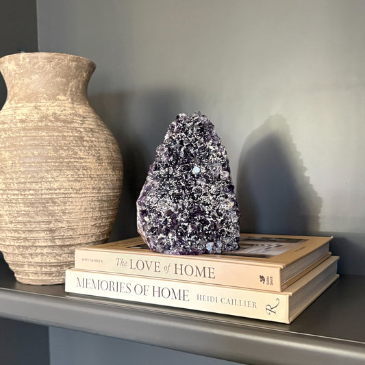 Decorative amethyst crystal rock and vase on a shelf.